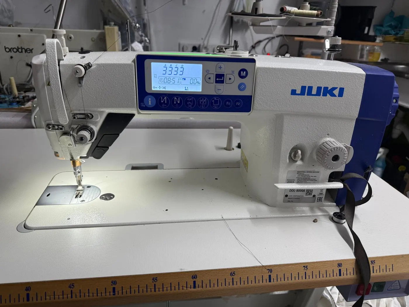 Industrielle JUKI DDL-8000A Nähmaschine auf der Werkbank der Änderungsschneiderei Toni in Köln, daneben ein integriertes Maßband am Tisch.